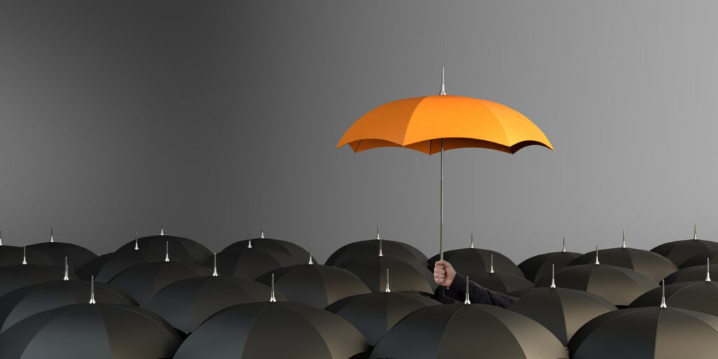 A sea of black umbrellas with one orange umbrella above them