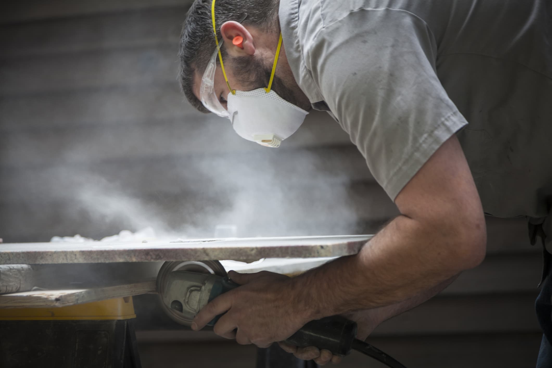 Male working a dangerous job that can cause a work injury, he is using a grinder to cut through stone