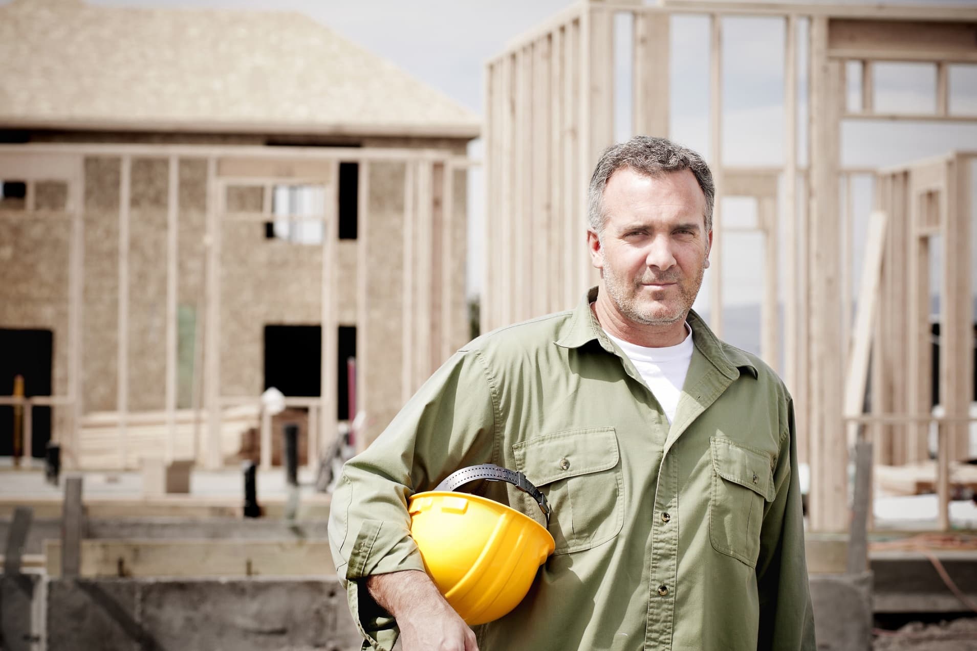 Building construction worker holding hardhat whilst on building site