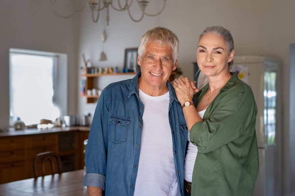 Husband and wife who cares for him at home smiling at camera